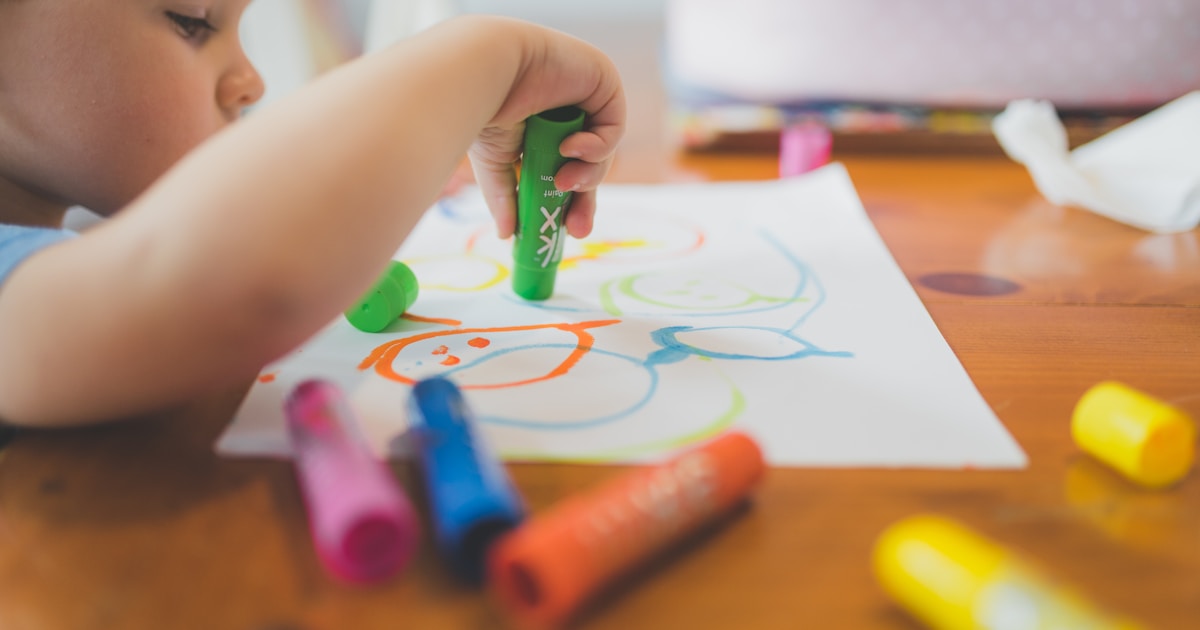 a little boy that is sitting at a table with some crayons