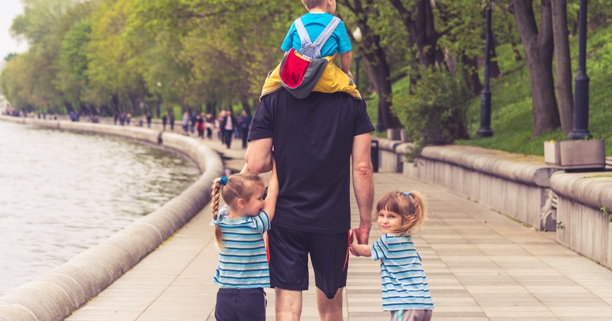 man in black t-shirt and brown shorts holding girl in blue and black jacket walking