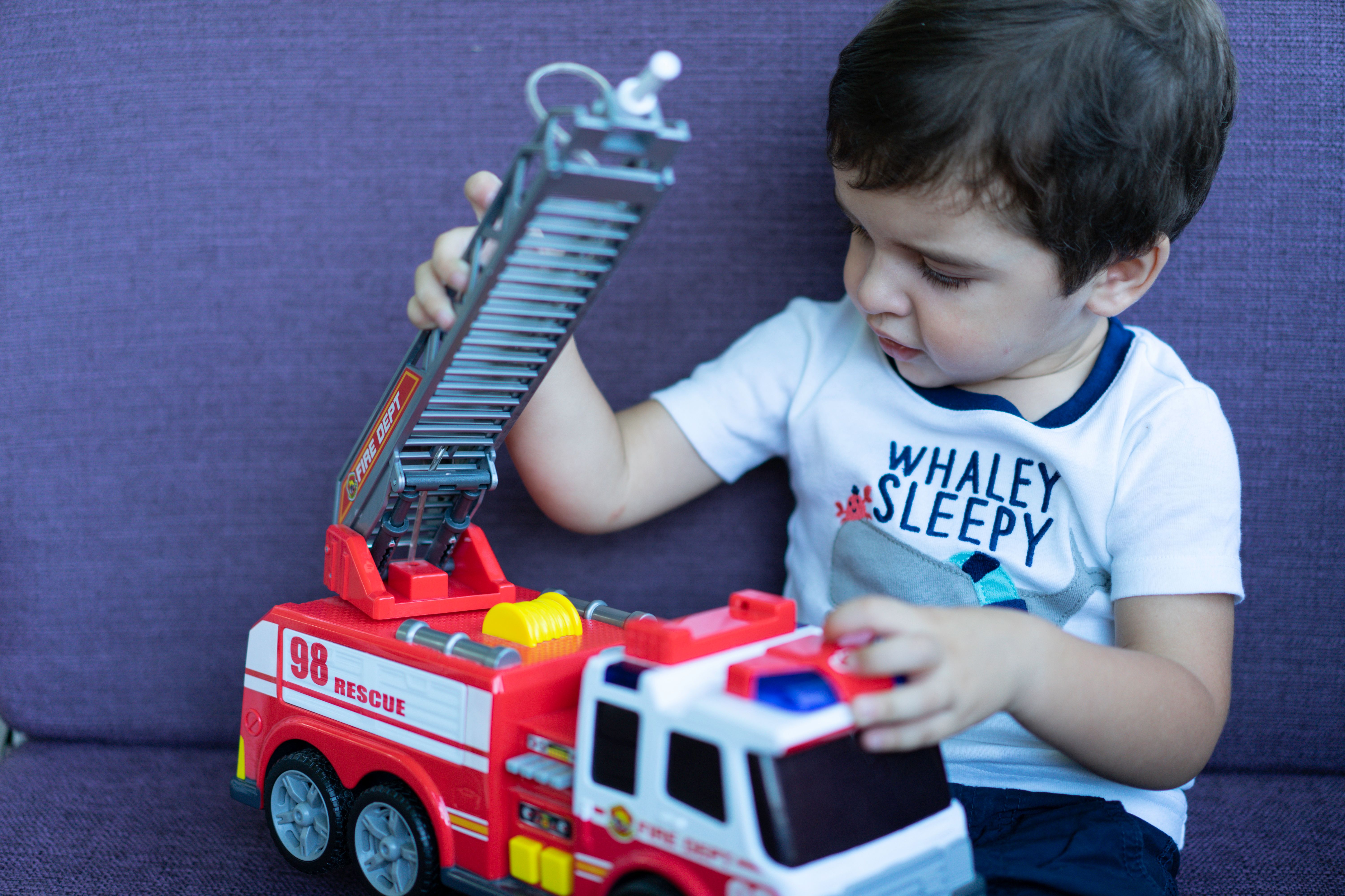 Toddler playing with a red toy fire truck on a couch